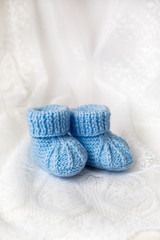 Fototapeta na wymiar Knitted blue baby booties on lace background