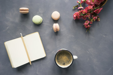 Fototapeta na wymiar Top view of notebook, coffee, macarons and flowers on cement background