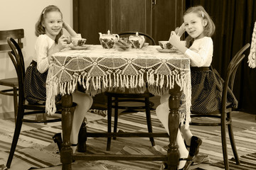 Girls Twins drinking tea at an antique table with a lace tablecl