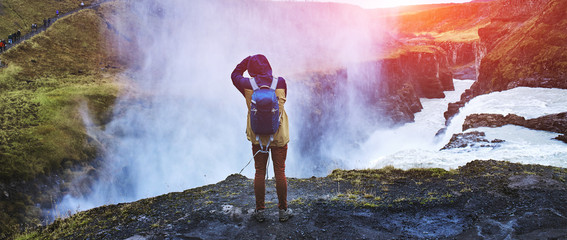 A man stands on the edge of a waterfall Gullfoss and takes pictures of him. Cloudy autumn day. Traveling in autumn in Iceland