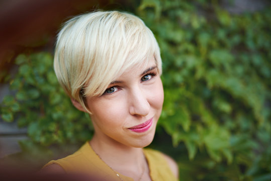 Attractive White Woman Taking A Selfie Against An Ivy Fence Backdrop