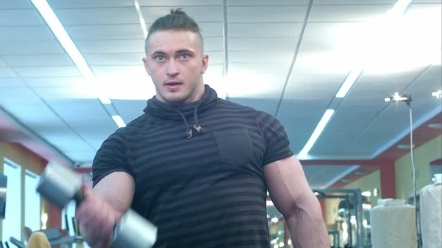 Powerful athletic man doing biceps exercise with dumbbells in a gym club