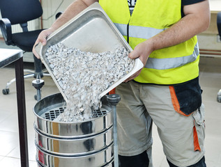 On site road testing laboratory. Placing sample of gravel into a silver container. Preparation step...
