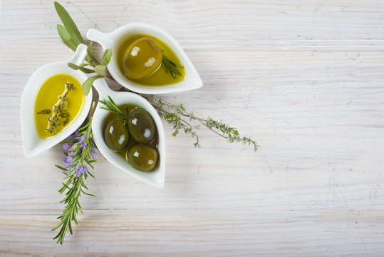 Aceite de oliva virgen extra y  aceitunas verdes aromatizadas con tomillo y romero sobre fondo de madera blanco