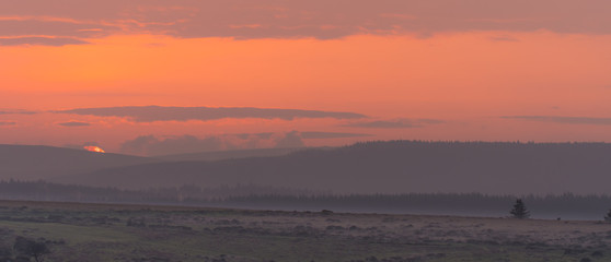 Sunset over Dartmoor National Park. Last moments of setting sun over Dartmoor Forest on misty evening in National Park in Devon, England, UK