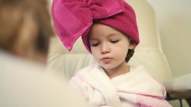 Pretty little girl in pink robe and towel on her head in professional salon