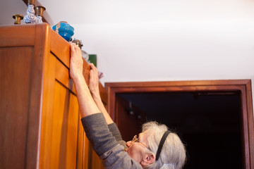 woman reaching for antique items on top of cupboard - Powered by Adobe