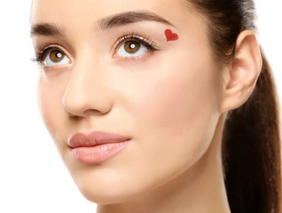 Beautiful young woman with heart painted on face against white background, closeup