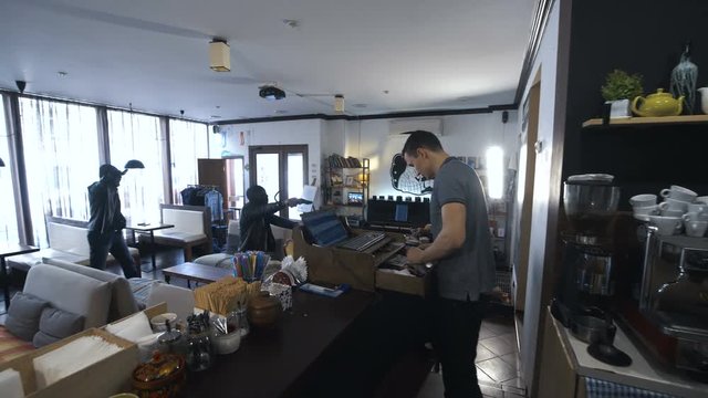 Two African people walking into the shop and aiming to the assistant with guns.