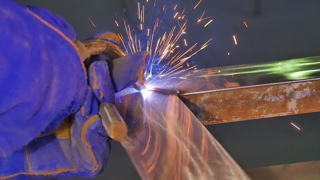 Metal Welding with sparks and smoke. Worker with protective mask welding metal. Welder joins metal parts. A process using a semi-automatic welding. Welding steel. Industrial Worker at the factory