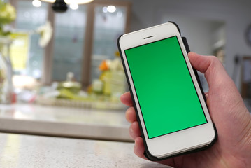 Woman holding green screen iphone with blurry dining room background
