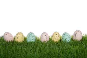 Row of pastel colored easter eggs splattered with speckles of paint laying on grass isolated on a white background.