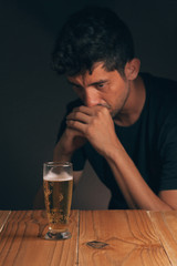 Concept of alcoholism. Sad man at the table with a glass of beer in a dark room.