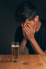 Concept of alcoholism. Sad man at the table with a glass of beer in a dark room.