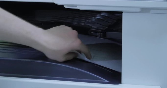 Man hands putting a sheet of paper into a copying device. Printer In Action. The printer prints paper. Print, copy and scan the business documents. man hand putting a sheet of paper out of copying