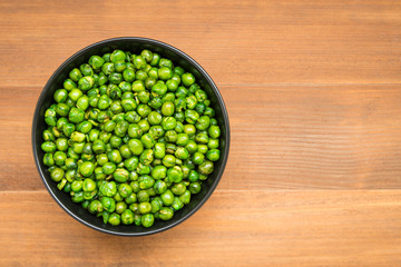 top view of roasted peas in bowl on wooden background