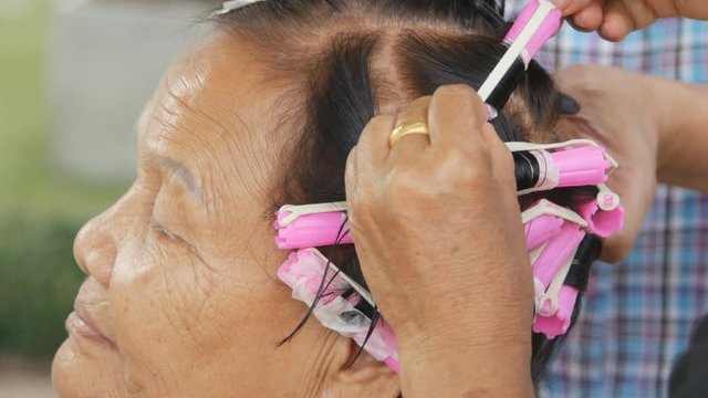 hand of a hairstylist doing a perm rolling the hair of senior woman