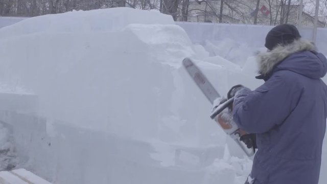View of sculptor carving ice. Movement. Cut ice with a chainsaw. Cut and make ice sculpture. Chopping ice with an axe. Ice Sculpture Carving. Chainsaw and snow. Master makes ice sculptures from ice