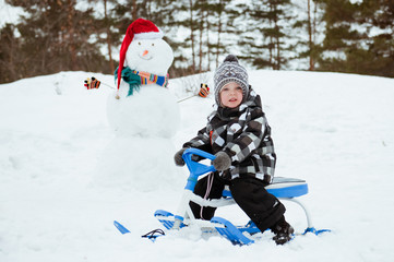 Fototapeta na wymiar Cute little boy in winter clothes outdoors. Child on a sled or snowmobile.