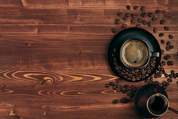 Hot coffee in black cup with crema, beans and turkish pot cezve with copy space on brown old wooden board background, top view.  Rustic style.