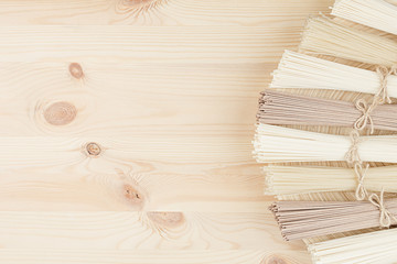 Bunch of different raw japanese noodles on wooden dish on beige board, top view. Decorative border with copy space.