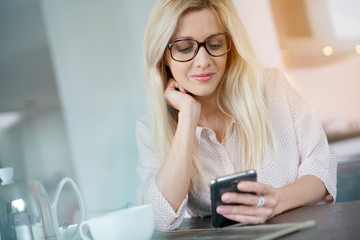 Blond woman with eyeglasses connected on smartphone at home