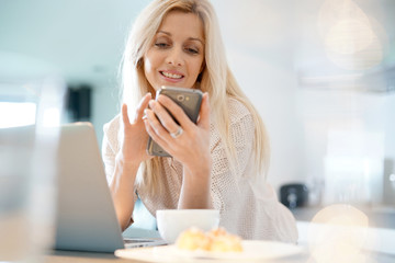 Blond woman with eyeglasses connected on smartphone at home