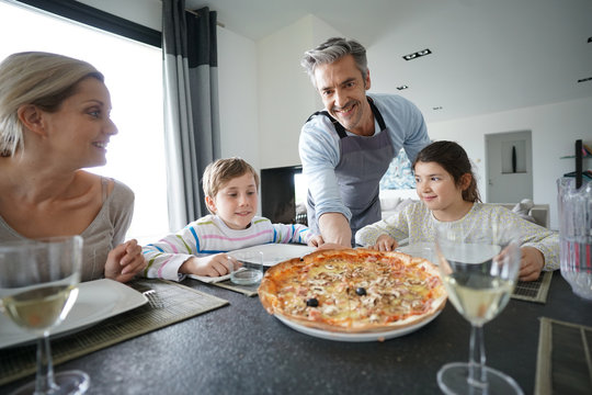 Dad serving pizza to family at dining table