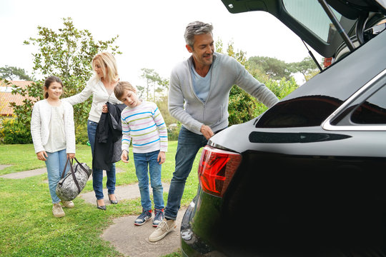 Family Of Four Loading Car Trunk To Leave For Vacation