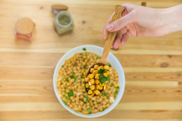 Spoonful of chick peas. Top view of cheak peas in wood spoon held in hand above the table and bowl...