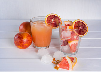 Full glass of grapefruit juice and glass of sliced fruit. Grapefruit sicilian orange with ice. White wooden background
