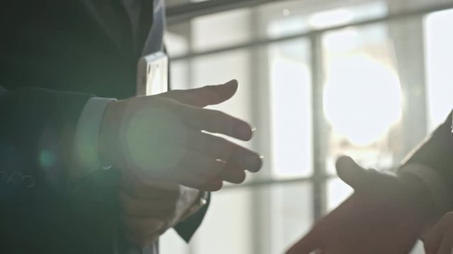 Mid-section shot with PAN of unrecognizable businessman with tablet standing in brightly lit workspace, shaking hands of business partners and discussing work