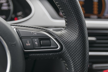 Fototapeta na wymiar media control buttons on the steering wheel in black leather modern car interior 