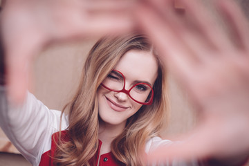 Stylish hipster woman with red eyeglasses making focus framing gesture and blinking
