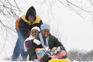African American brothers and sister sliding on a sled.