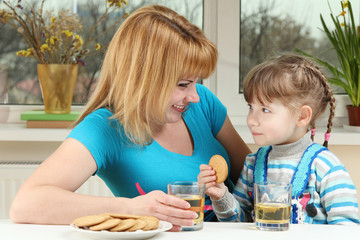 Mom and daughter drinking juice with biscuits