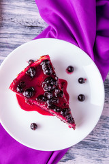Piece of cheesecake on white plate with currant on colored wooden background. Top view