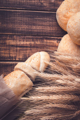 Different kind of freshly baked bread on a rustic wooden table near wheat. Healthy eating concept. Copy space