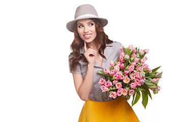 Beautiful girl in hat with flowers tulips in hands on a light background