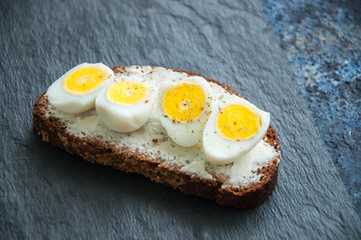 Rye bread bruschetta.  Quail Eggs and cream Cheese sandwich served on a stone board on blue background. Close up.