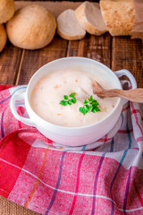 Cream soup in white bowl with wood spoon near bread on wooden background. Rustic style.