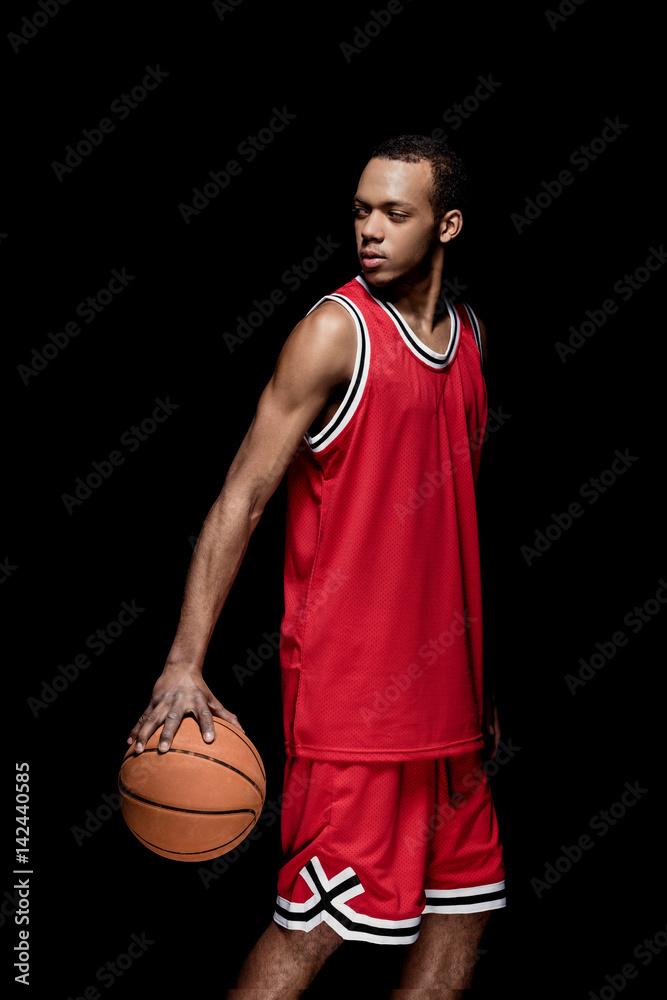 Wall mural young african american sportsman standing with basketball ball on black