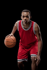 Young sportsman in uniform playing basketball with ball on black