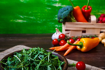 Arugula leaves in bowl. Fresh salad. Carrot, pepper and cherry tomatoes. Natural raw vegetables. Organic bio food on rustic wooden table.
