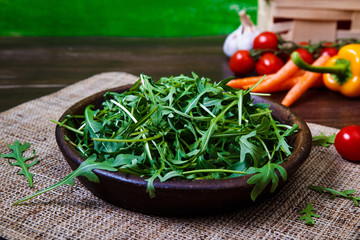 Arugula leaves in bowl. Fresh salad. Carrot, pepper and cherry tomatoes. Natural raw vegetables. Organic bio food on rustic wooden table.