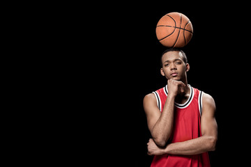 Young confident basketball player posing with ball on head on black