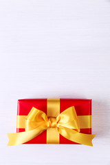 Gift box with yellow bow. Present wrapped with ribbon. Christmas or birthday red package. On white wooden table.