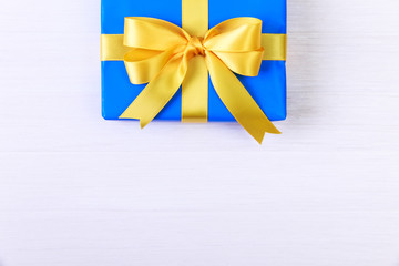 Gift box with yellow bow. Present wrapped with ribbon. Christmas or birthday blue package. On white wooden table.