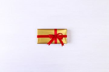 Gift box with red bow. Present wrapped with ribbon. Christmas or birthday golden paper package. On white wooden table.