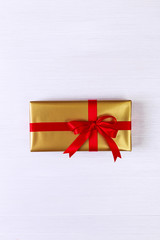 Gift box with red bow. Present wrapped with ribbon. Christmas or birthday golden paper package. On white wooden table.
